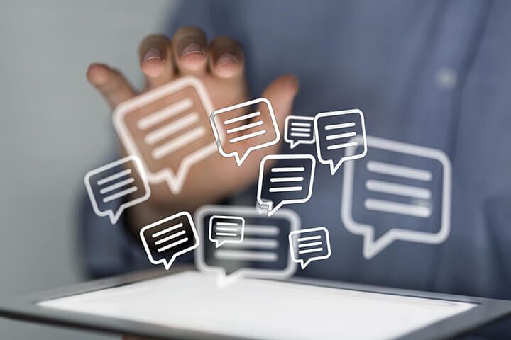 Person interacting with a tablet, displaying floating chat bubbles symbolizing digital communication.